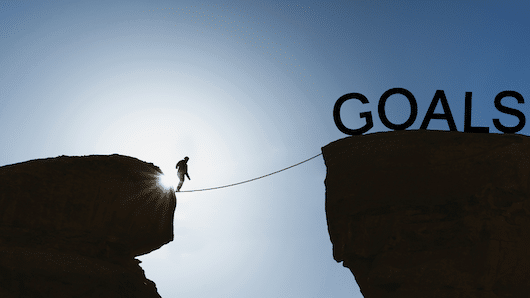 Un entrepreneur ambitieux en train de marcher sur une corde au dessus d'une falaise. Il marche pour atteindre ses objectifs